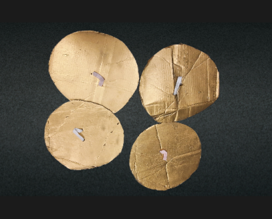 Four golden handmade cymbals with white handles in a greyish-black background