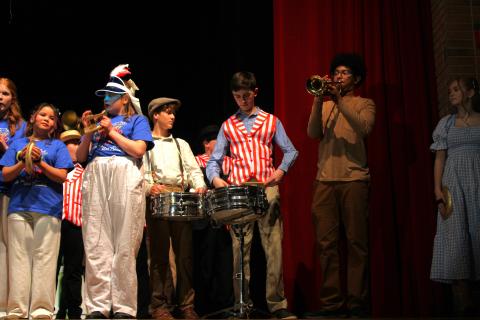 Music Man band characters holding instruments and playing them, including drums, trumpets, and cymbals.