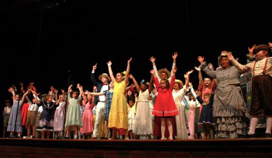 Music Man characters in 1912 clothing on stage dancing.