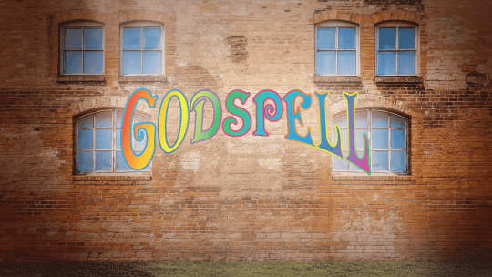 A curtain warmer of a brick building with windows and the Godspell logo in rainbow lettering