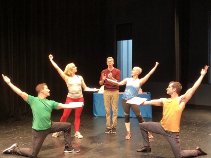 Choreography Guides for Disney's the Little Mermaid A man in a maroon shirt in the middle of four dancers, two on either side with their arms stretched upwards.