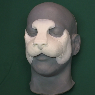 A foam latex housecat nose prosthetic placed on a platic human face cast.