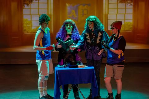 A group of four young adults standing in front of a blue table reading a book
