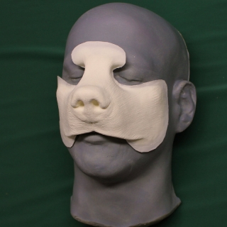 A foam latex bear nose prosthetic placed on a platic human face cast.