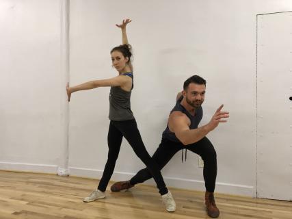 A female dancer with one arm up and one arm outstretched and a male dancer lunging forward with his arm outstretched.