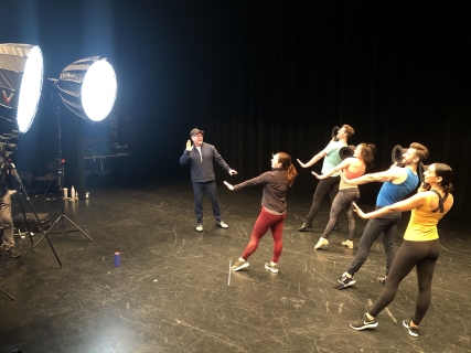 Choreography Guides for Beauty and the Beast A choreographer demonstrating a move as four dancers behind perform the movement in front of bright lights.