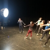 A choreographer demonstrating a move as four dancers behind perform the movement in front of bright lights.