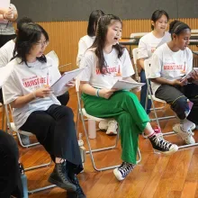 Kids rehearse a Camp Broadway show, seated in chairs while reading their scripts.