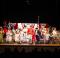 Music Man characters in 1912 clothing on stage dancing.