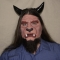 A man wearing a foam latex beast face prosthetic with makeup, beard and horns.